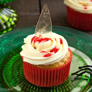 Single broken glass cupcake with sugar shard and strawberry syrup blood on green plate.