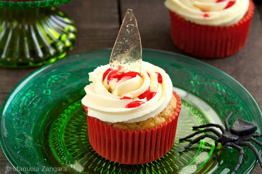 Broken glass Halloween cupcake with shard and red syrup on green glass plate.