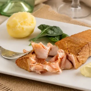 Tea smoked salmon served with boiled potatoes, spinach, and homemade aioli on a white plate.
