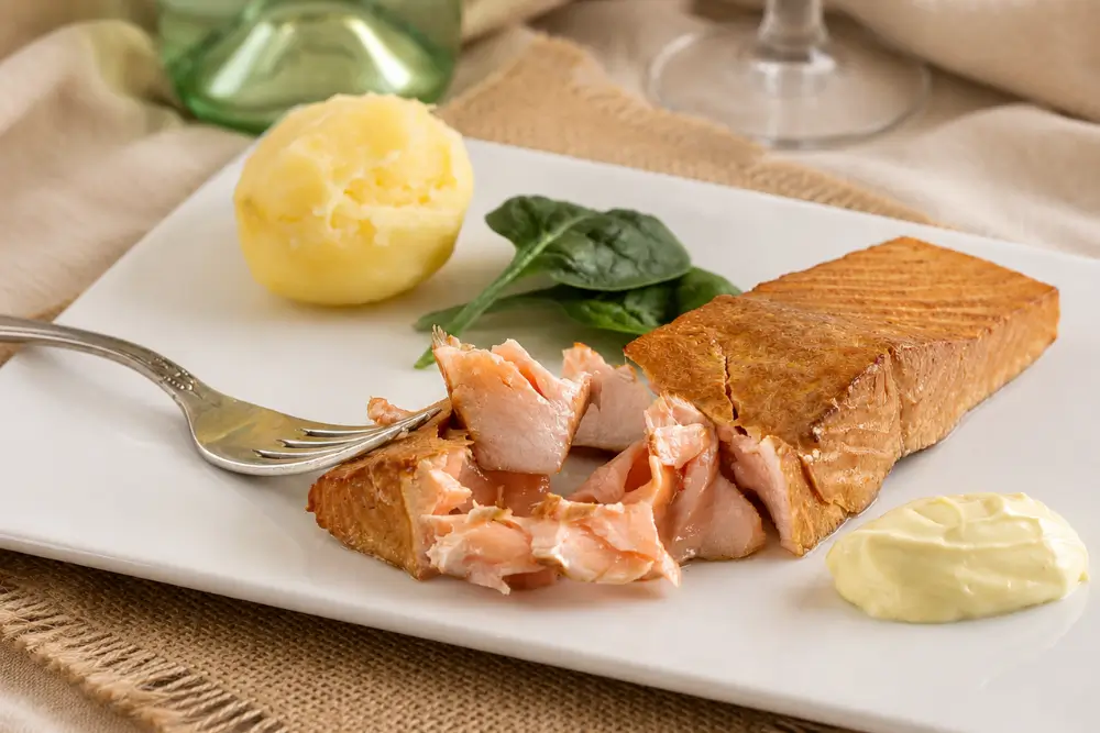 Tea smoked salmon served with boiled potatoes, spinach, and homemade aioli on a white plate.