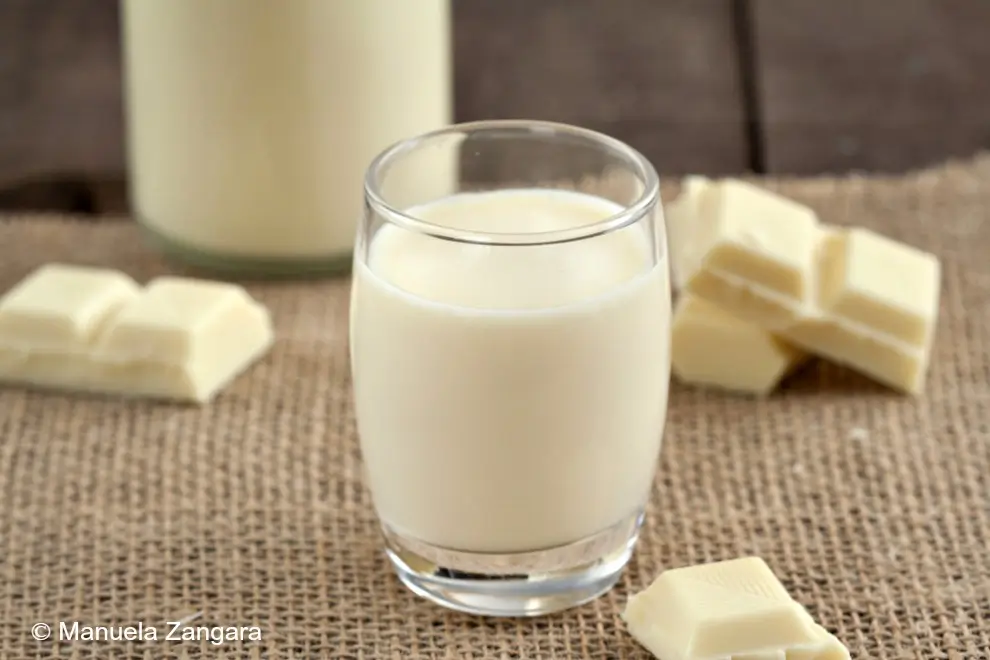 Close-up of homemade white chocolate liqueur in a glass on a textured surface.