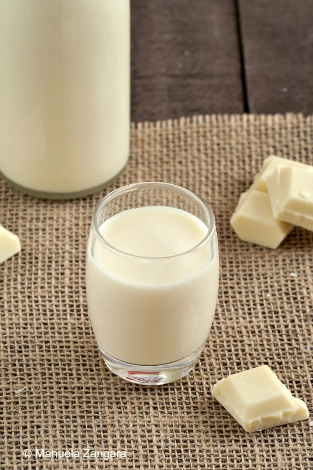 Glass of homemade white chocolate liqueur with chocolate pieces on a rustic surface.
