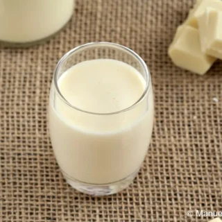 Small glass of homemade white chocolate liqueur surrounded by white chocolate squares.