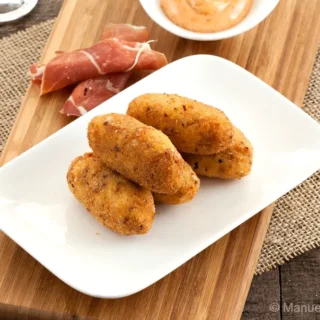 Crispy Serrano croquettes on a plate with paprika mayo and sliced ham.