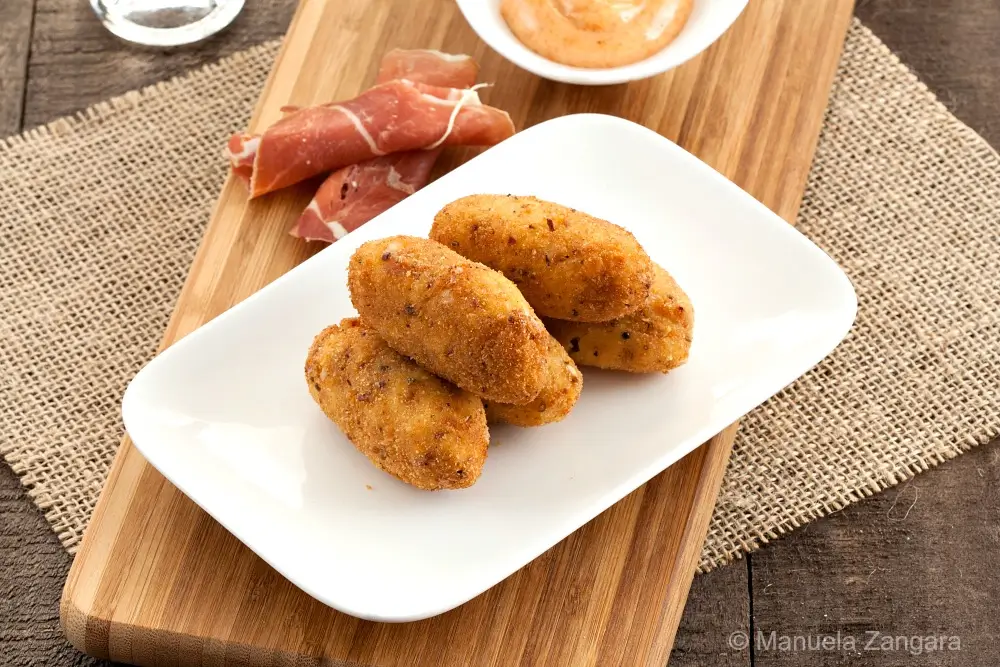 Crispy Serrano croquettes on a plate with paprika mayo and sliced ham.