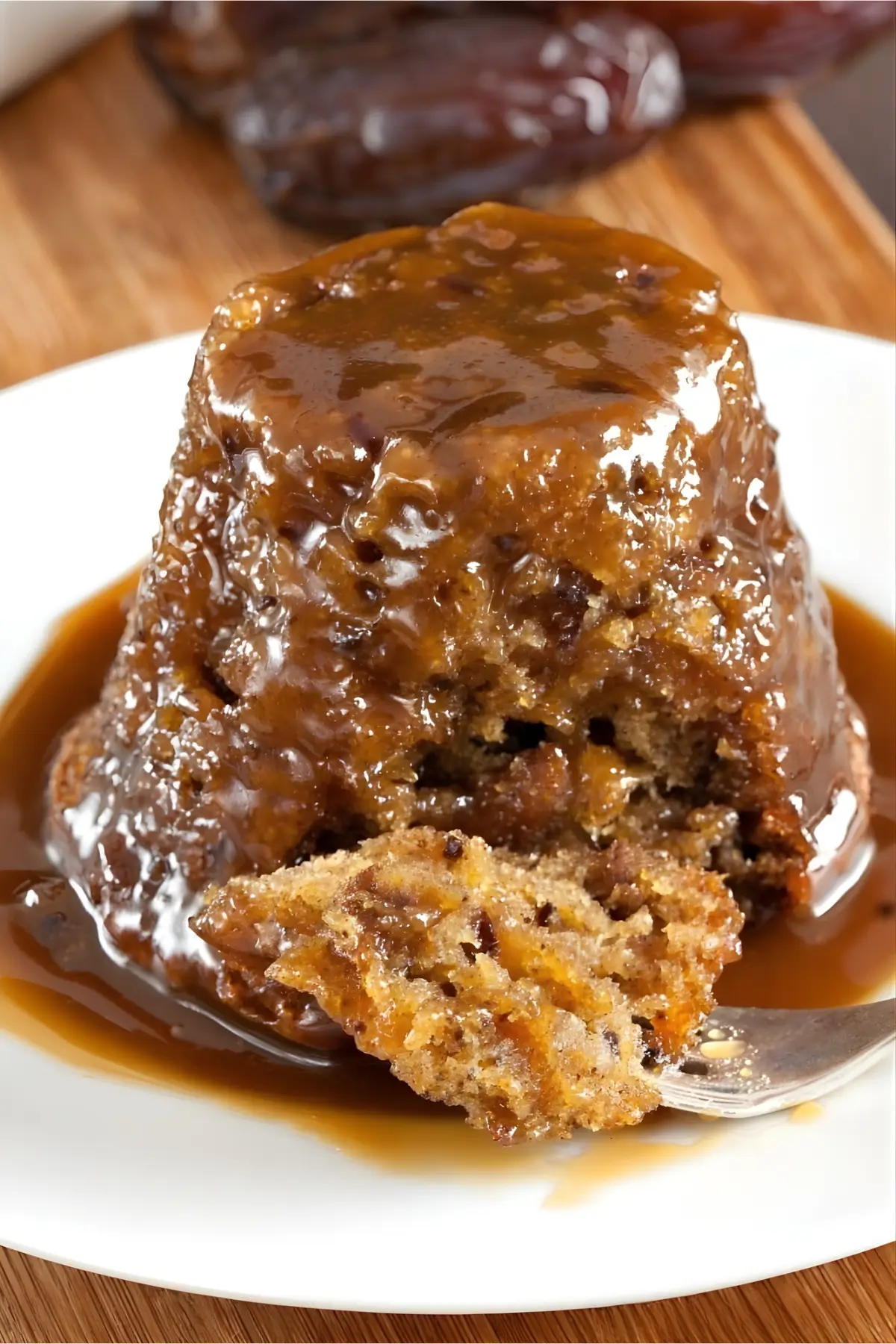 Sticky date pudding topped with warm butterscotch sauce, with a spoonful cut out.