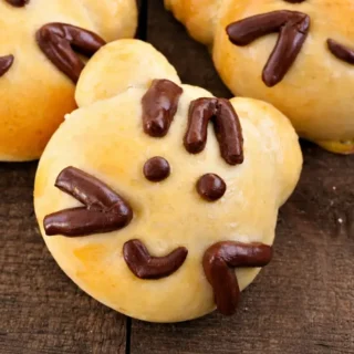 Baked Kitty Cat Bread Buns with chocolate dough facial details on a wooden surface.