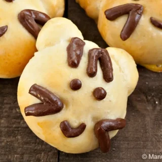 Baked Kitty Cat Bread Buns with chocolate dough facial details on a wooden surface.