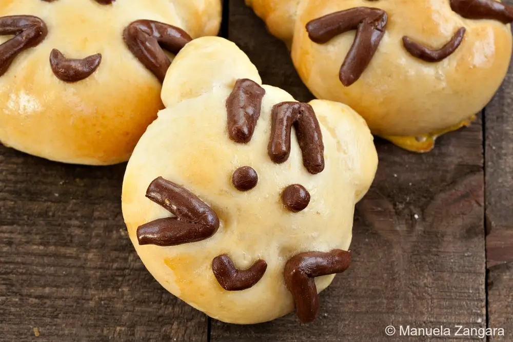 Baked Kitty Cat Bread Buns with chocolate dough facial details on a wooden surface.
