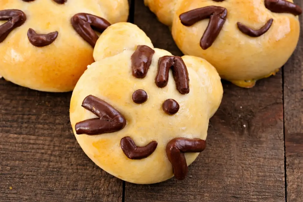 Baked Kitty Cat Bread Buns with chocolate dough facial details on a wooden surface.