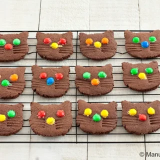 Chocolate cat cookies cooling on a wire rack, decorated with bright candy pieces.