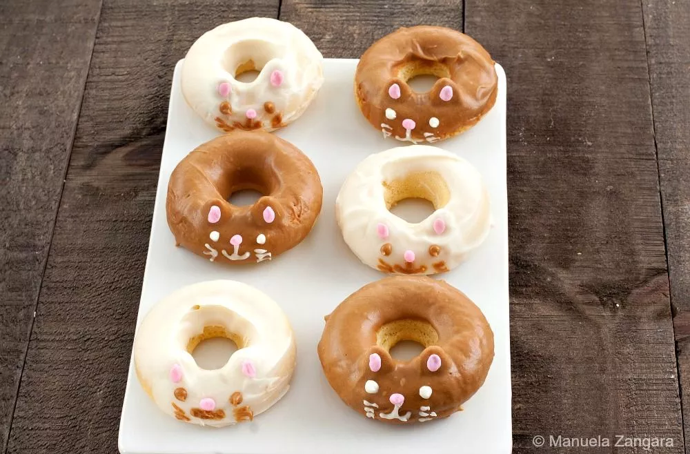 Six kitty cat doughnuts on a tray, decorated with chocolate and white glaze.