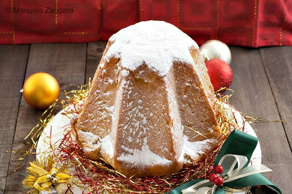 Whole Pandoro dusted with icing sugar, placed on a festive plate decorated with ribbons and tinsel.