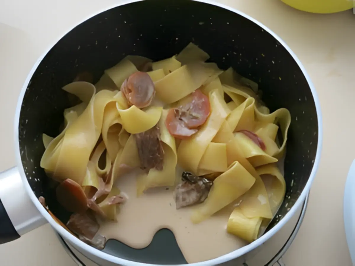 Pappardelle mixed with carrot and porcini cream sauce in a saucepan.