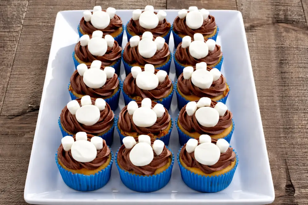 Paw patrol cupcakes topped with chocolate icing and marshmallow paw decorations on a tray.