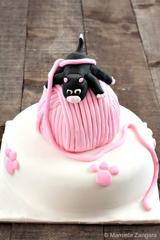 Detailed view of the fondant kitten with pink nose and white paws lying over the yarn ball.