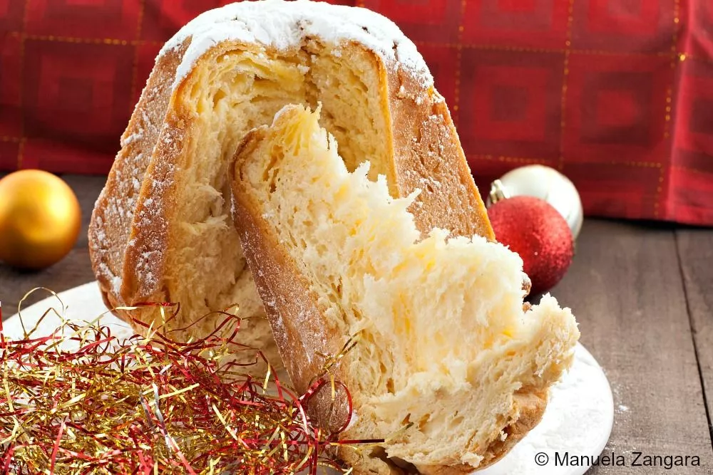 Pandoro sliced open to reveal its soft, airy crumb and golden crust, dusted with icing sugar and surrounded by festive decorations.