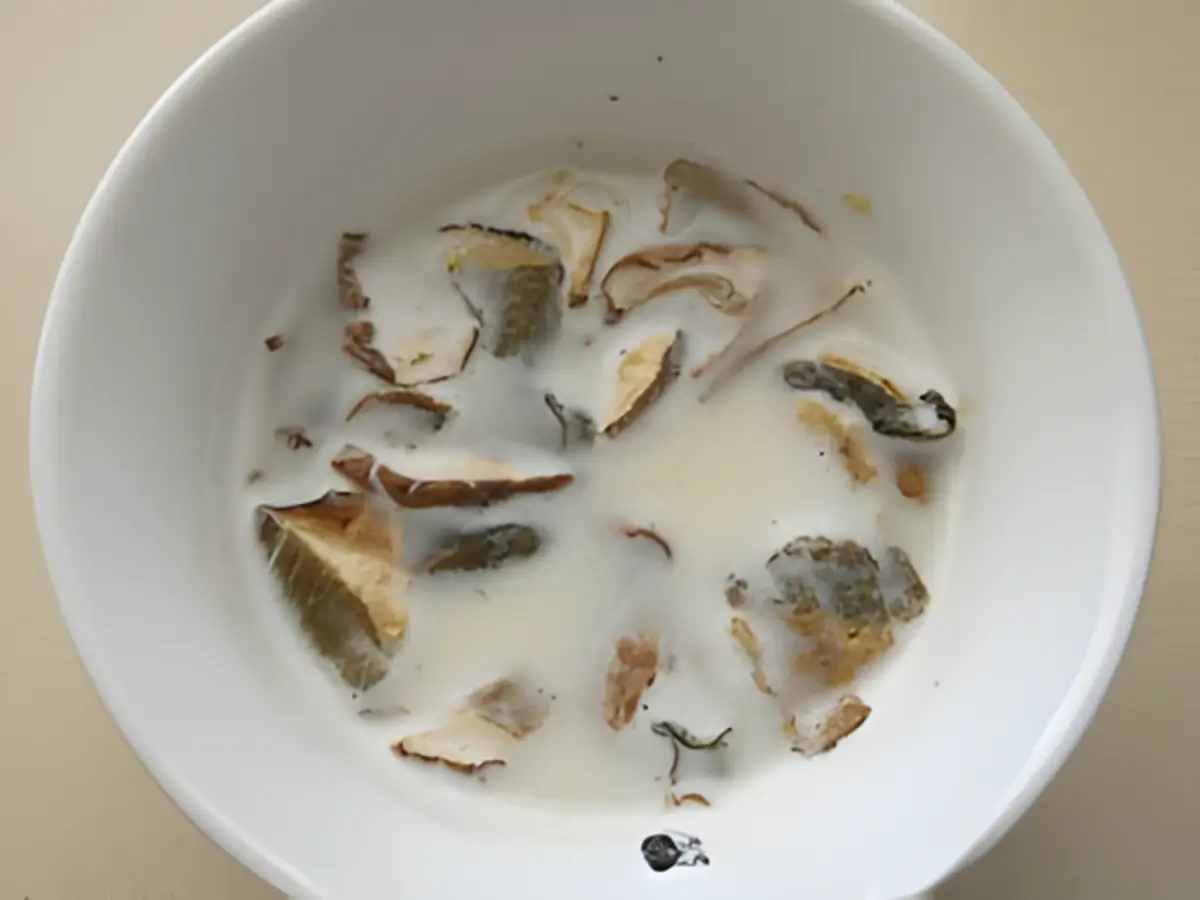 Dried porcini soaking in hot water and milk in a white bowl.