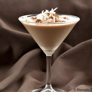 Sweet Dreams Cocktail served in a martini glass, topped with whipped cream, cocoa powder, and coconut shavings.
