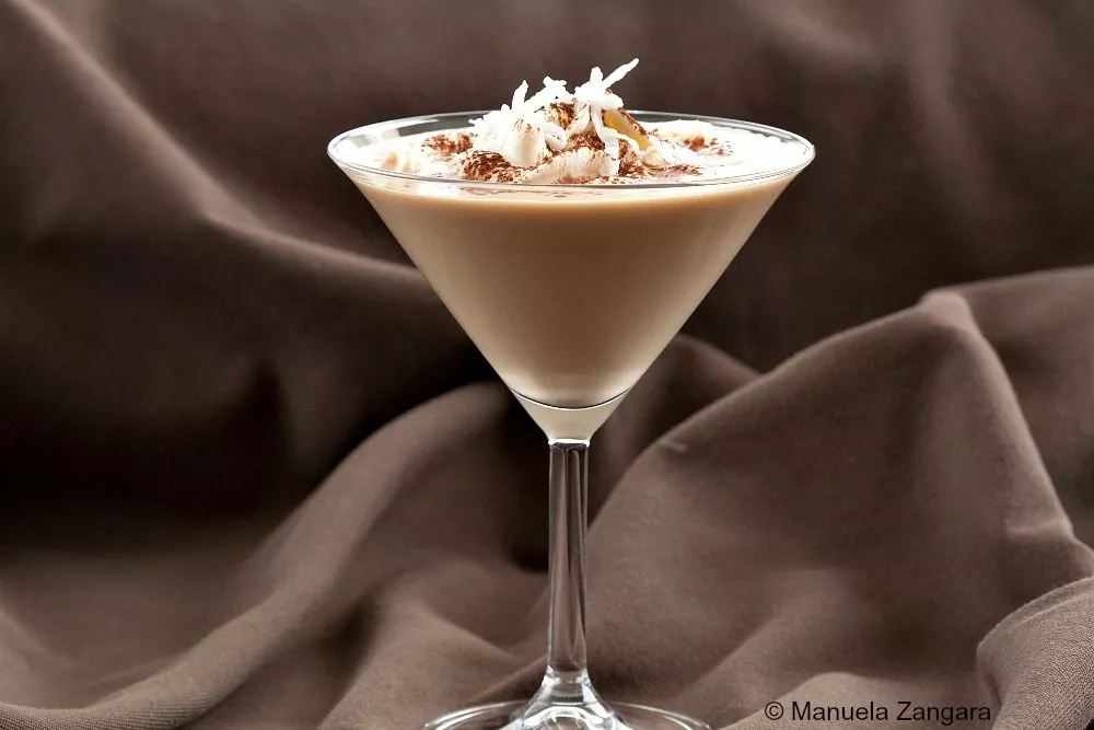 Sweet Dreams Cocktail served in a martini glass, topped with whipped cream, cocoa powder, and coconut shavings.