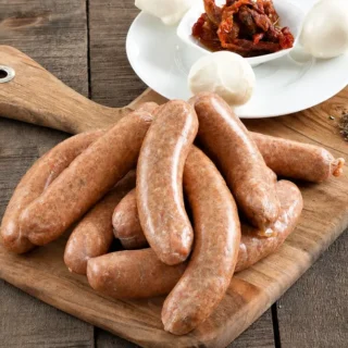 Mozzarella and Sun-Dried Tomato Pork Sausages on a wooden board with mozzarella and Sun-Dried tomatoes.