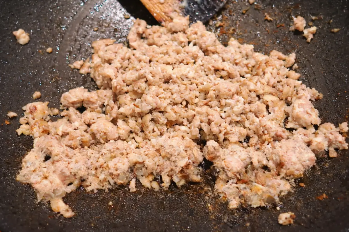Ground chicken cooking in a wok until lightly browned and crumbly.