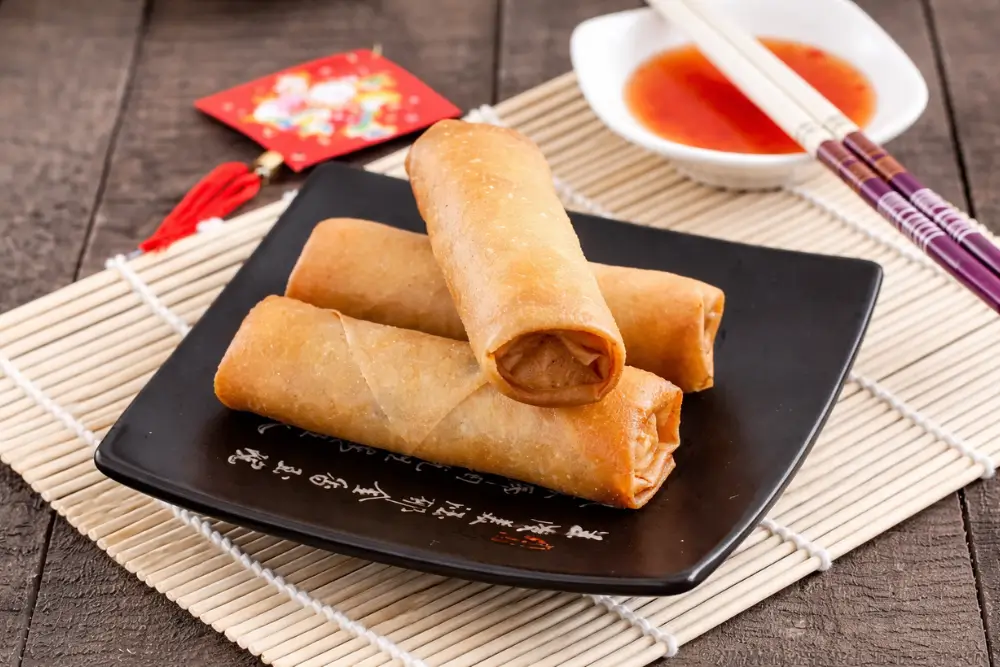 Golden fried chicken spring rolls stacked on a black plate with dipping sauce.