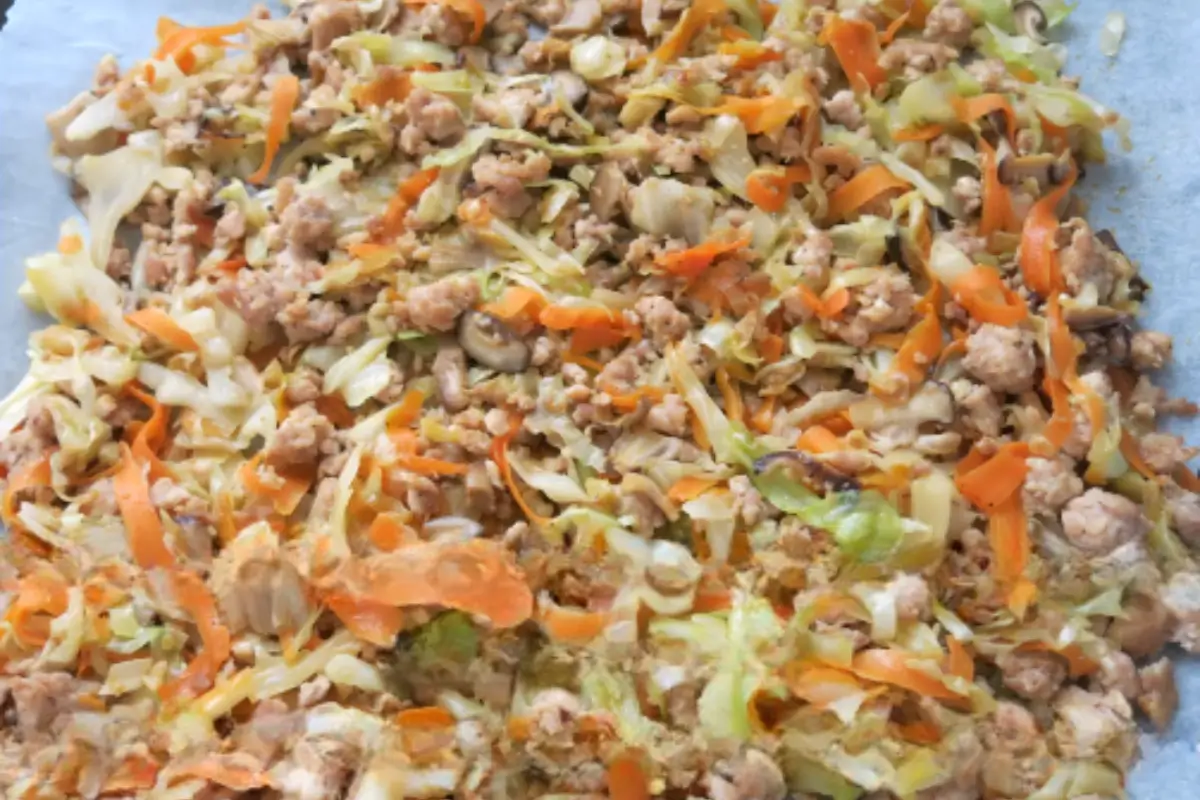 Cooked chicken mixed with cabbage, carrots, and mushrooms spread out to cool.
