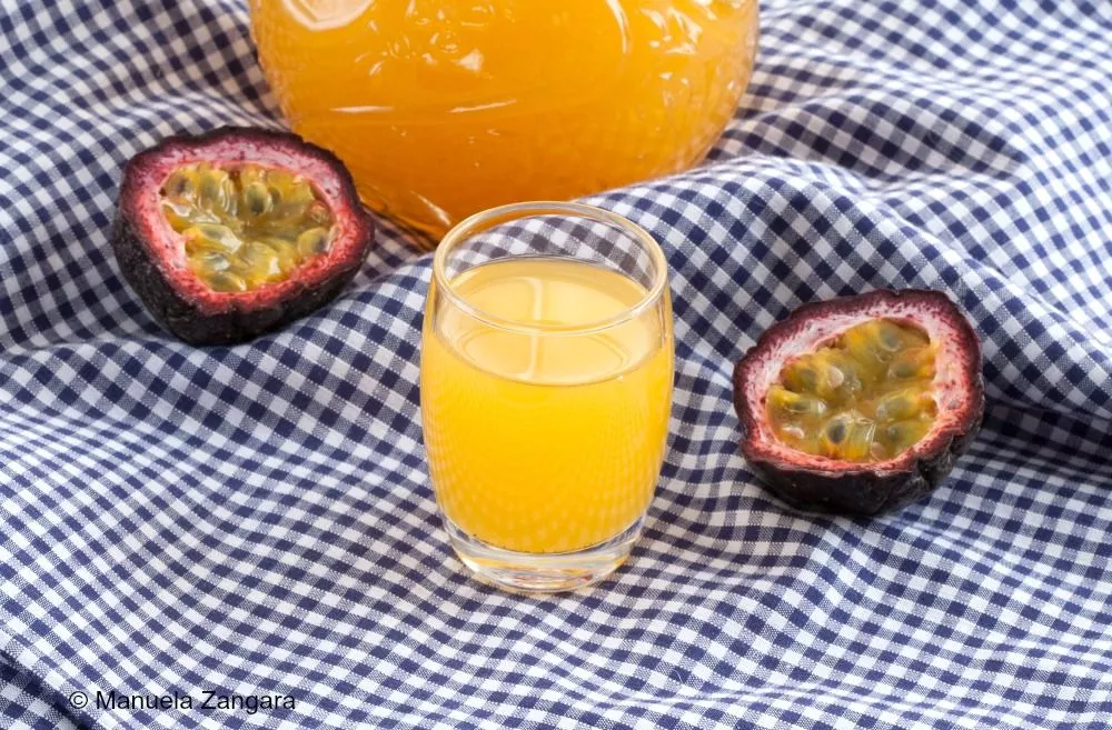 Close-up view of a glass filled with golden Passion Fruit Liqueur surrounded by fresh passion fruit.