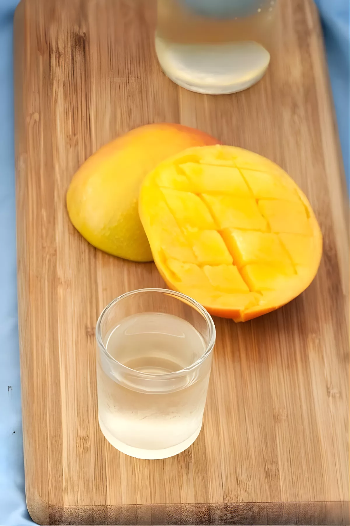 Clear glass of Mango Liqueur on a wooden board with fresh sliced mango for garnish.