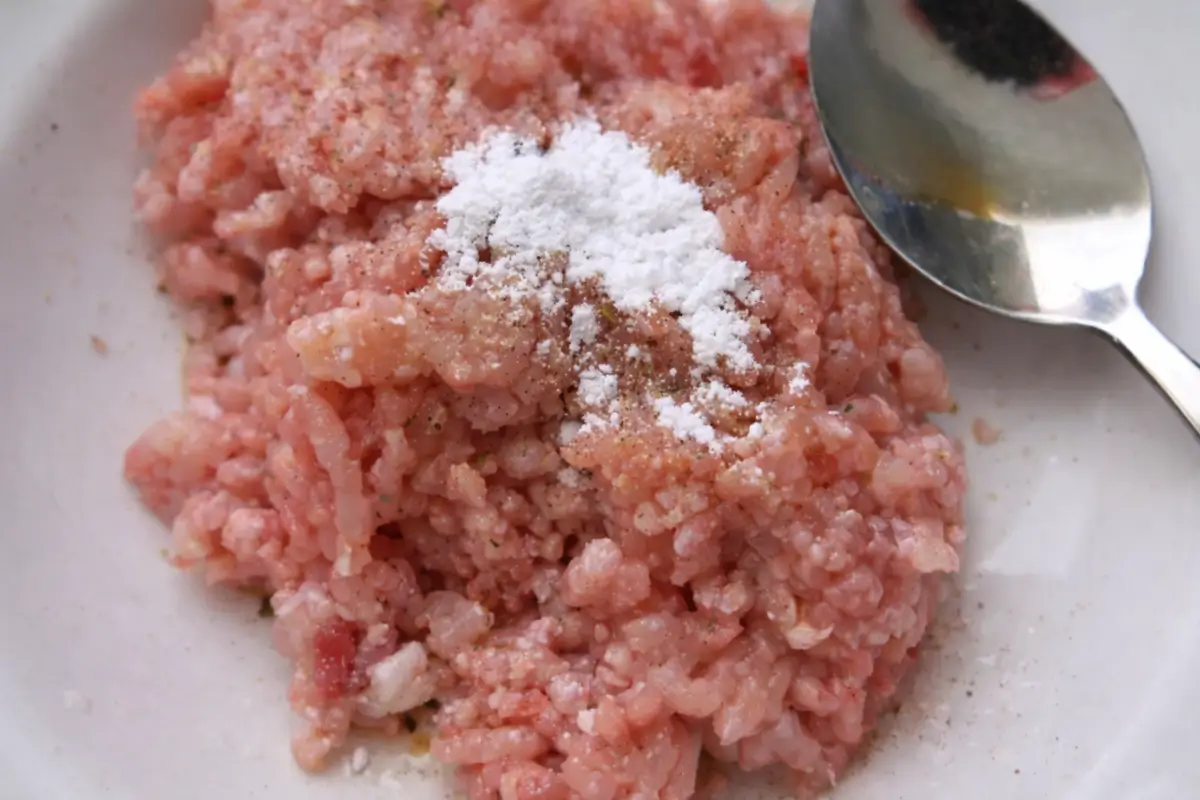 Ground chicken mixed with seasoning and cornstarch in a bowl before cooking.