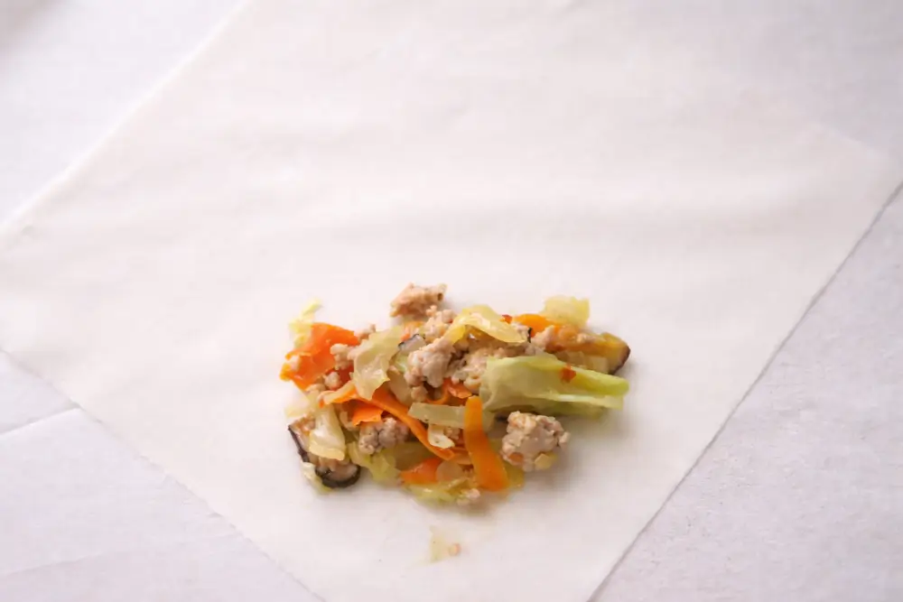Spoonful of chicken and vegetable filling placed on a spring roll wrapper before rolling.