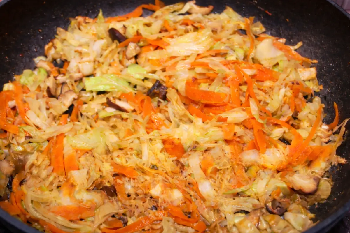 Cabbage, carrots, and mushrooms cooking together in a wok for the spring roll filling.