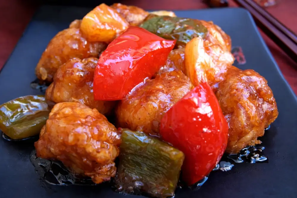 Sweet and sour pork fritters coated in glossy sauce with red and green peppers.