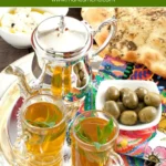 Moroccan mint tea served in glasses with flatbread, olives, and cheese on a colourful tray.