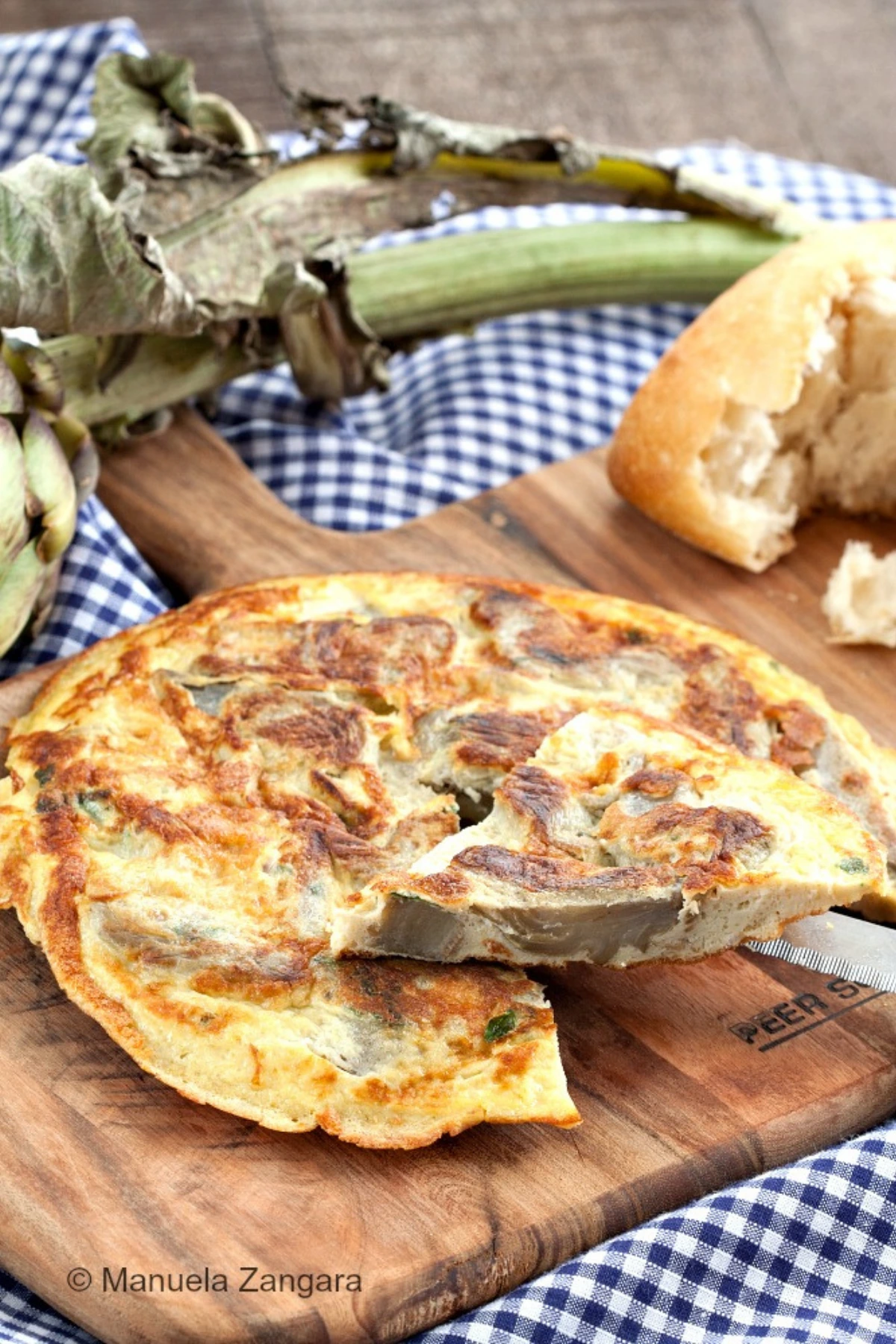 Sliced artichoke frittata on a serving board with rustic bread and fresh artichokes.