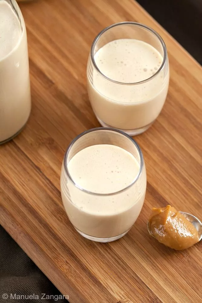 Close-up of Homemade Dulce de Leche Liqueur in two glasses beside a bottle.
