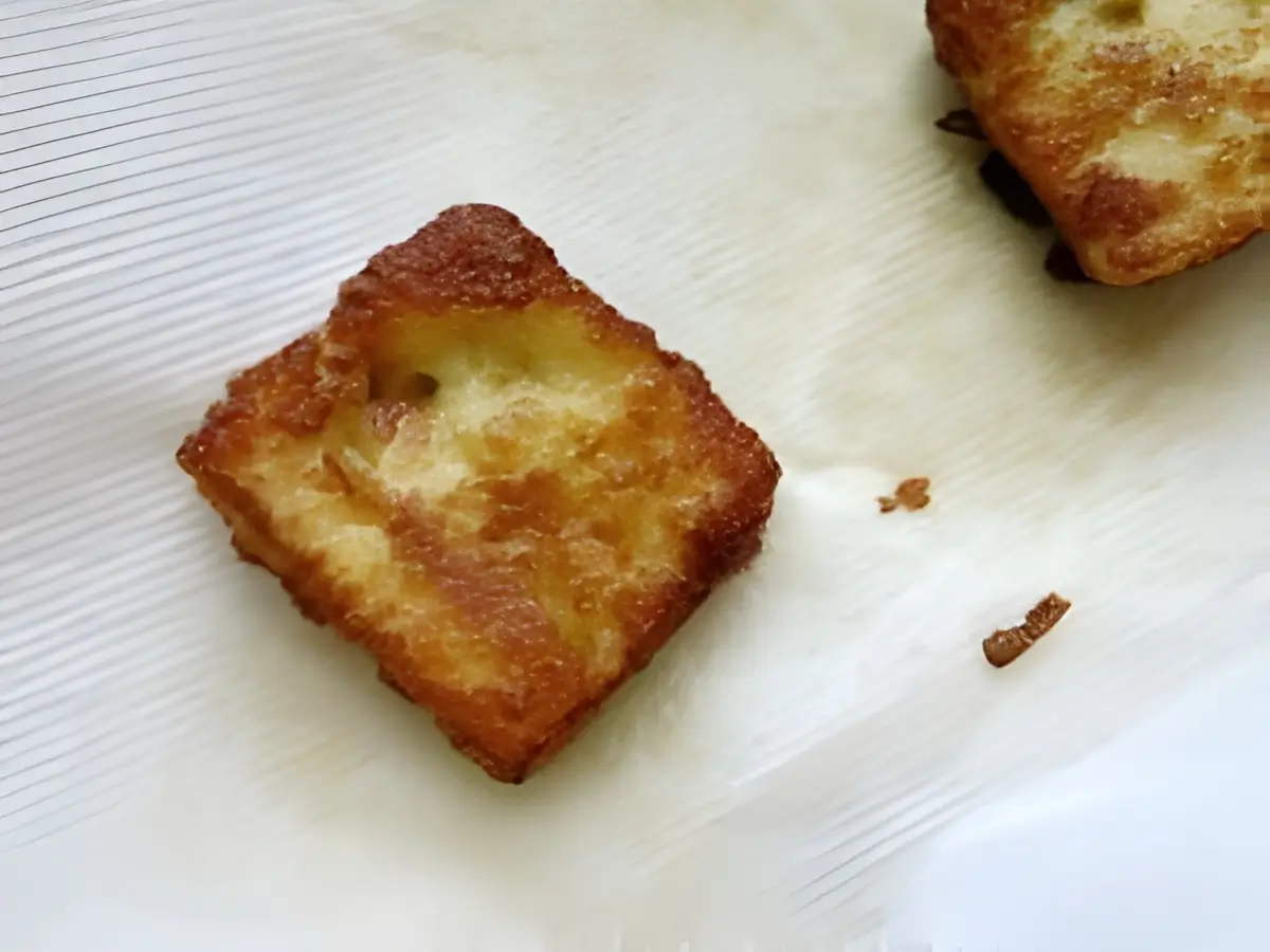 Close-up of crispy halloumi cheese square cooling on paper towel after frying.