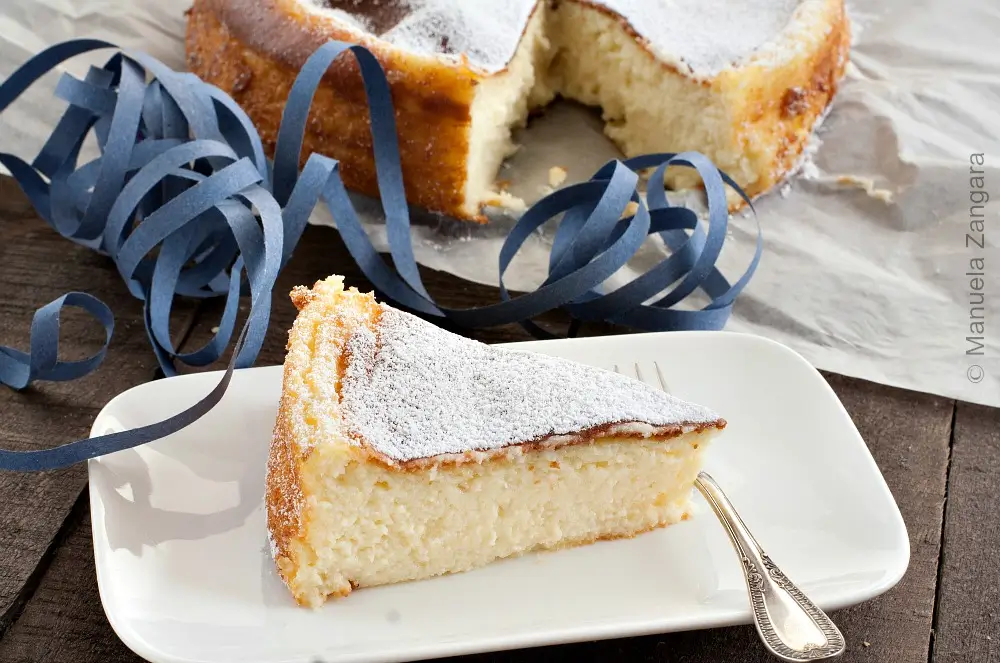 Close view of the baked cake topped with powdered sugar on a wooden table.