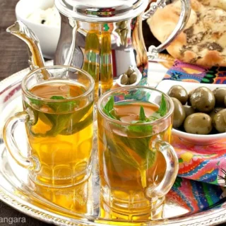 Moroccan mint tea served in glasses with flatbread, olives, and cheese on a colourful tray.