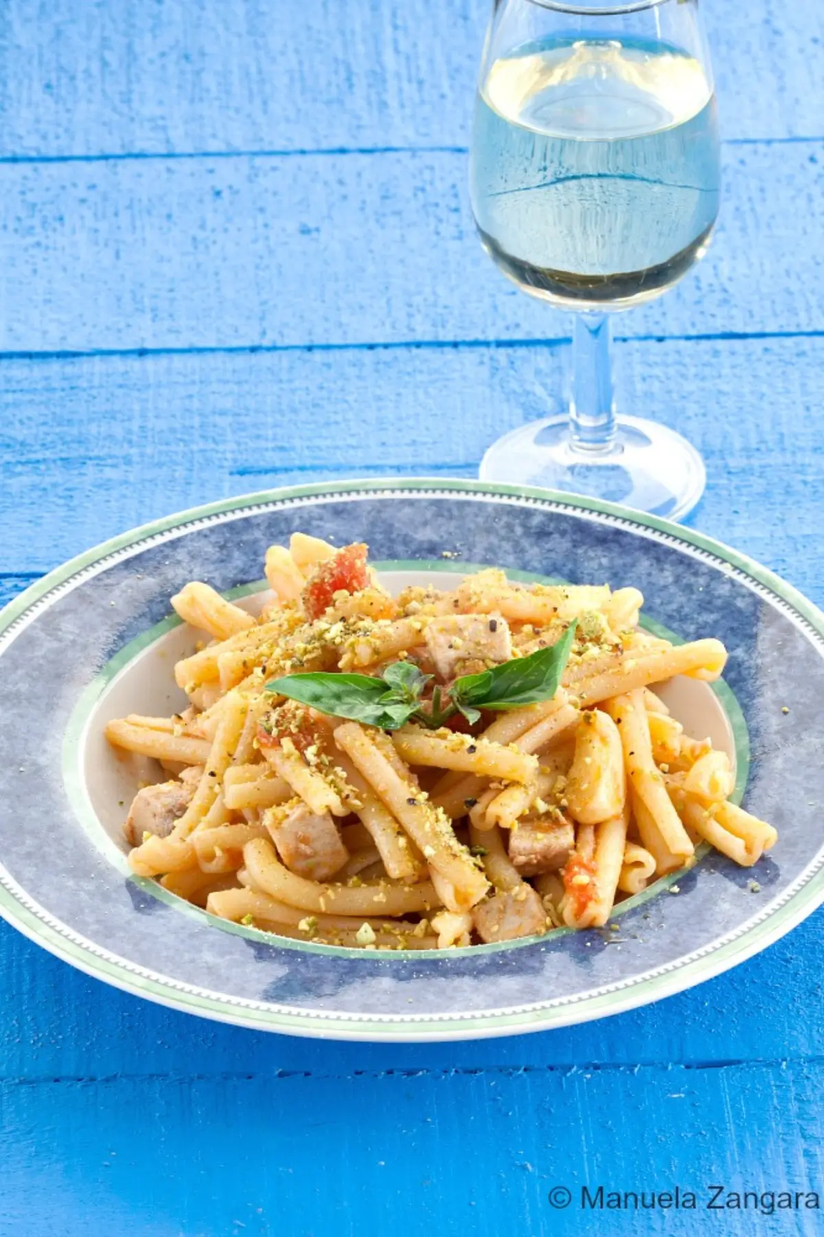Swordfish and pistachio pasta served on a blue table.