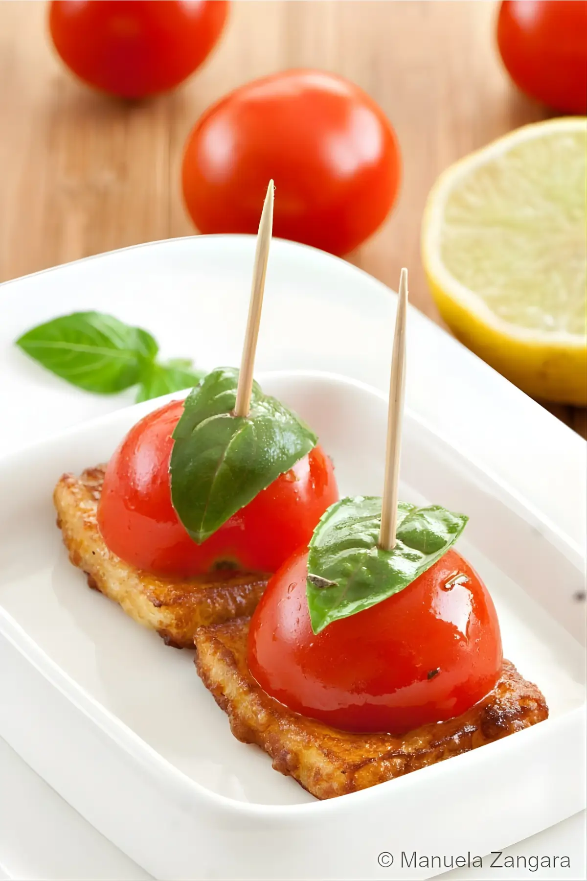 Two cherry tomato and basil skewers on fried halloumi with lemon and fresh basil in the background.