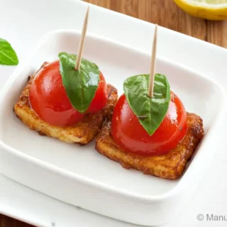 Tomato and basil skewers on halloumi squares served on a white dish.