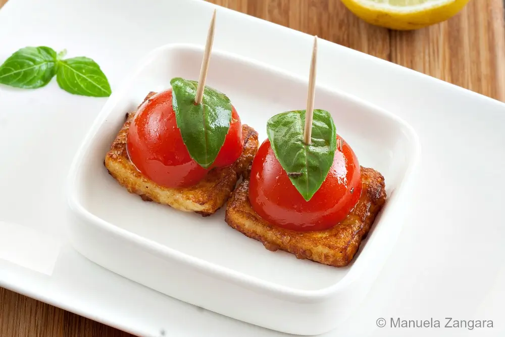 Tomato and basil skewers on halloumi squares served on a white dish.