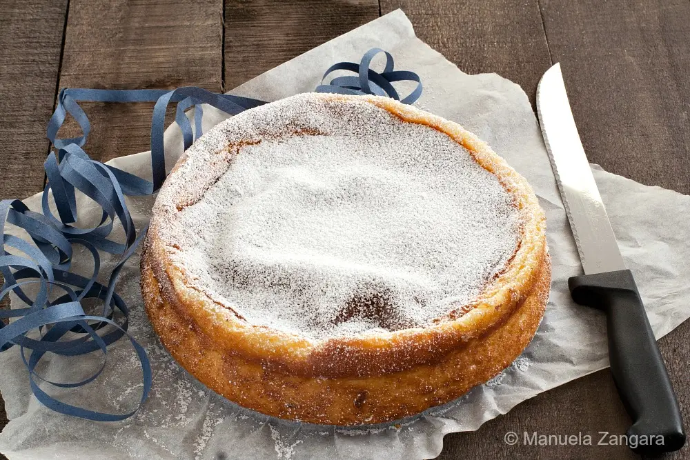 Whole ricotta and semolina cake dusted generously with icing sugar on baking paper.