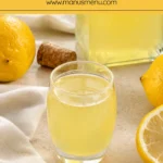 Glass of homemade limoncello with fresh lemons on a light stone surface.