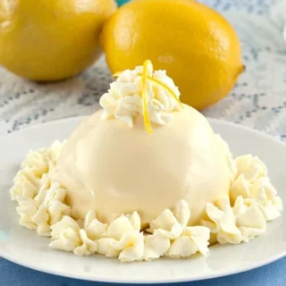 Finished Delizia al Limone, an Italian lemon dessert topped with whipped cream and lemon zest, served on a white plate.