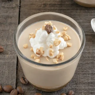 Glass of coffee mousse topped with whipped cream, chopped hazelnuts, and a coffee bean.