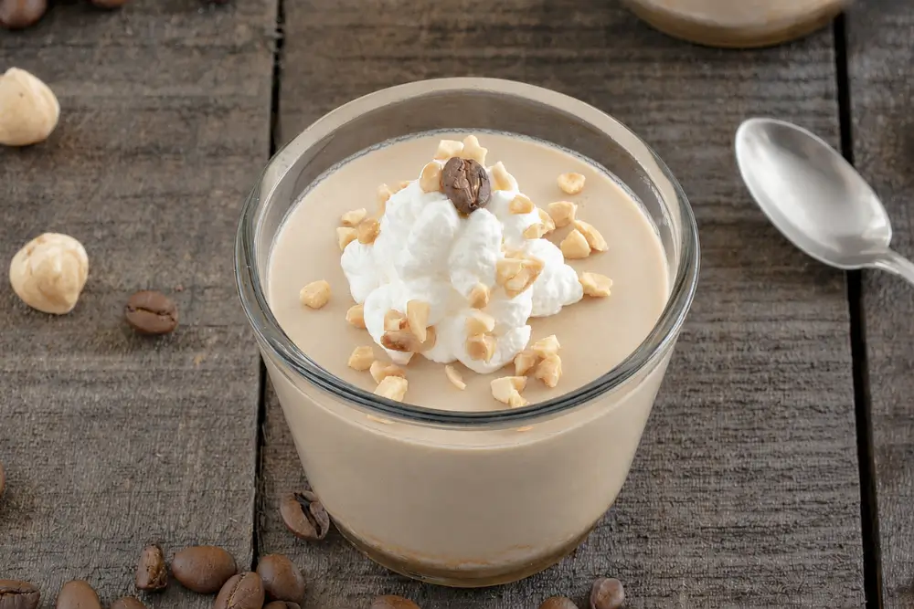 Glass of coffee mousse topped with whipped cream, chopped hazelnuts, and a coffee bean.
