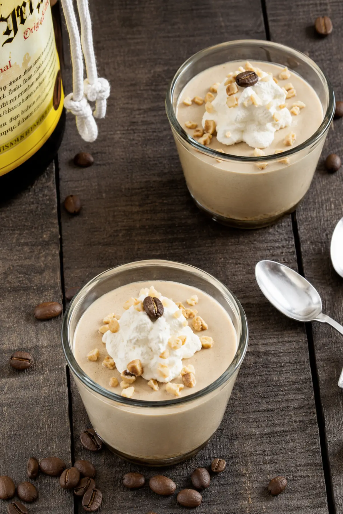 Two glasses of espresso mousse served with whipped cream, hazelnuts, coffee beans, and spoons.